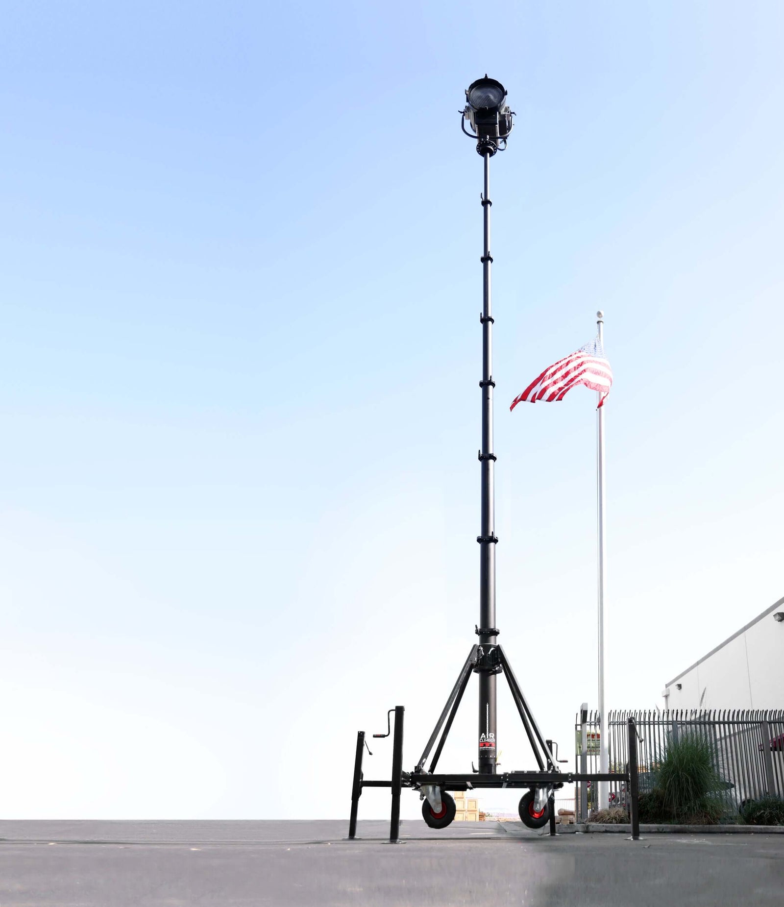 Tall mobile lighting tower next to an American flag against a clear blue sky.