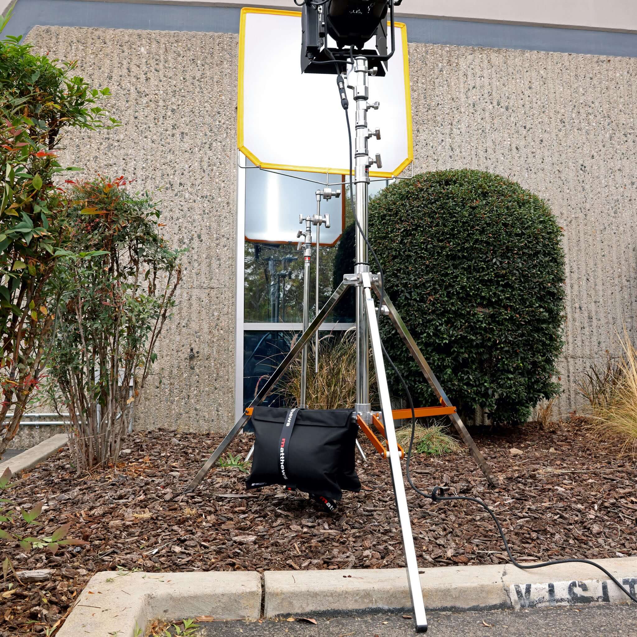 Professional lighting equipment set up outdoors, featuring a stand, softbox, and balanced weight bag.