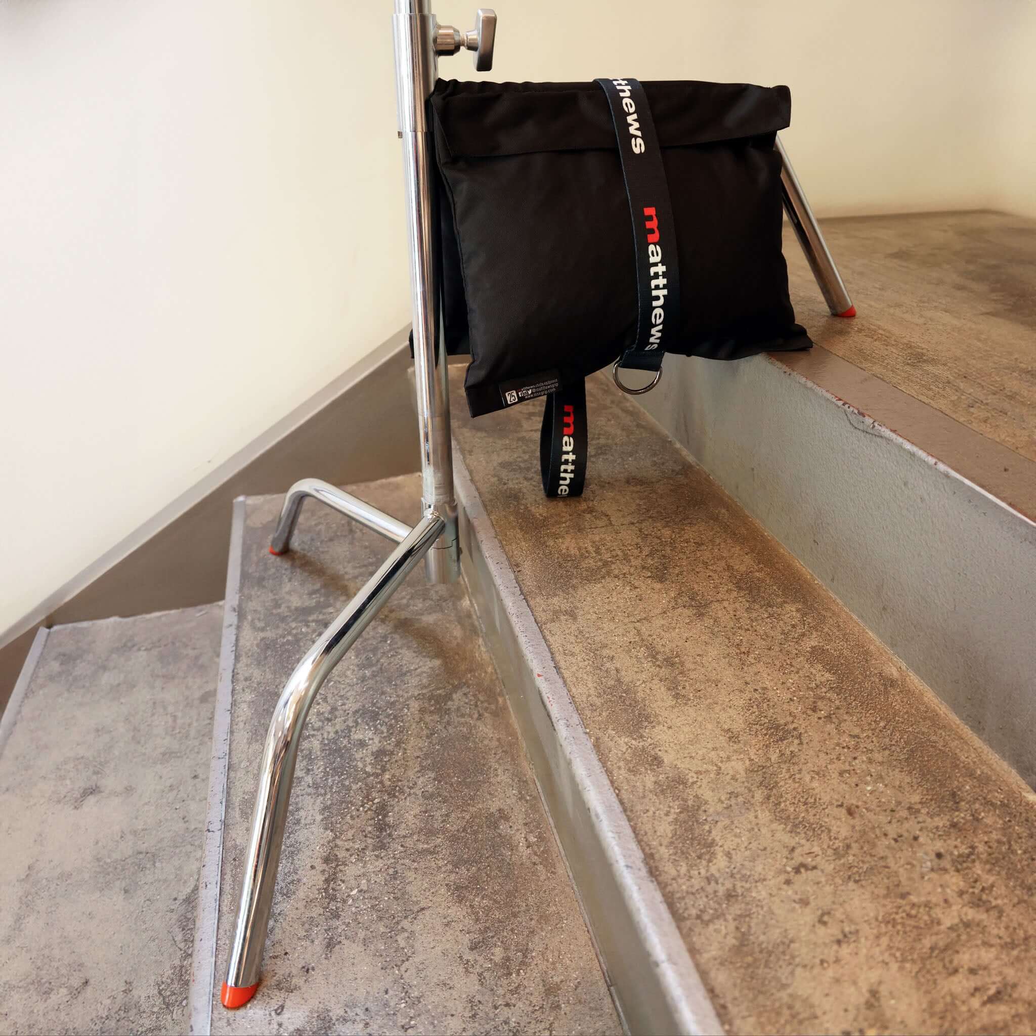 Black bag by Matthew Williams resting on stairs with a metal holder, showcasing modern design and urban style.