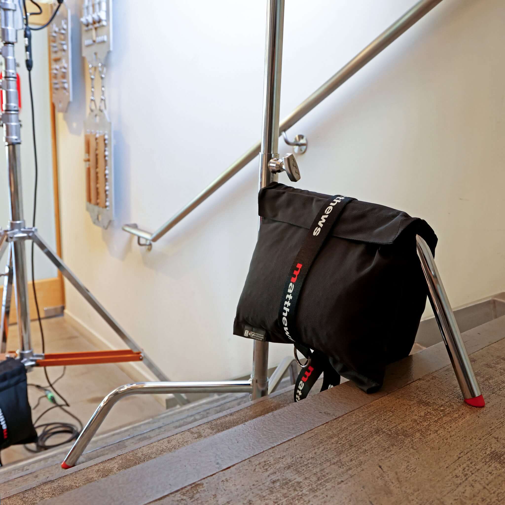 Black Matthews gear bag resting on a stair railing, showcasing filming equipment in a studio environment.