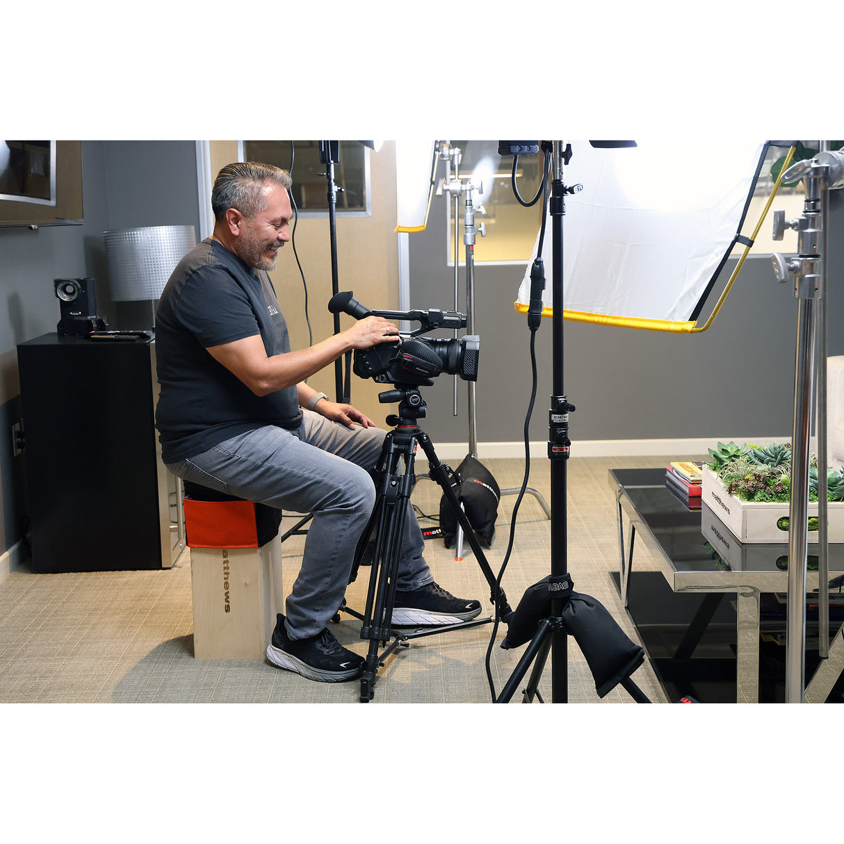 Videographer using camera while seated comfortably on Apple Box Topper by Matthews on a film set