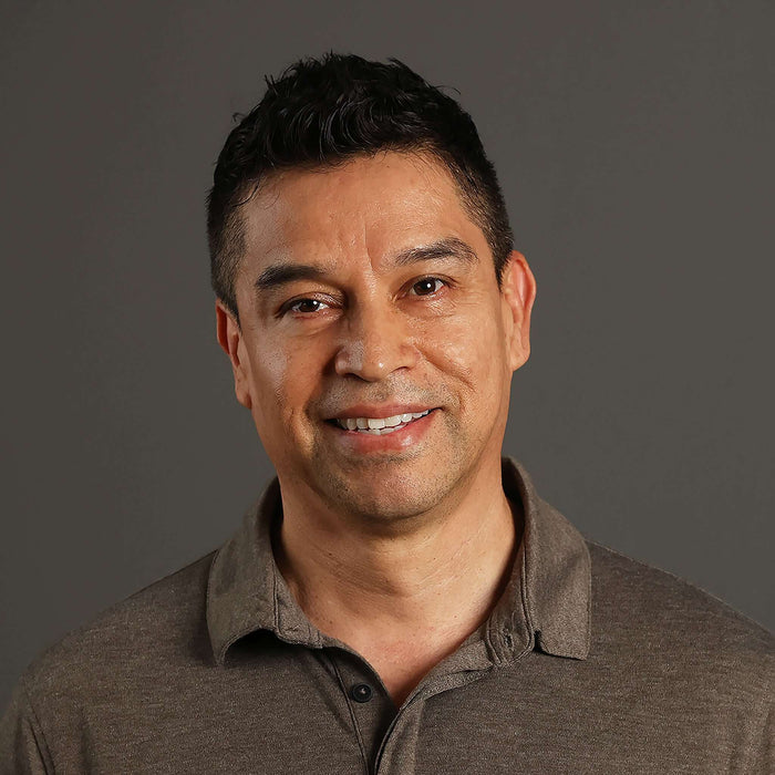 Smiling man in a gray polo shirt against a neutral background, showcasing confidence and approachability.