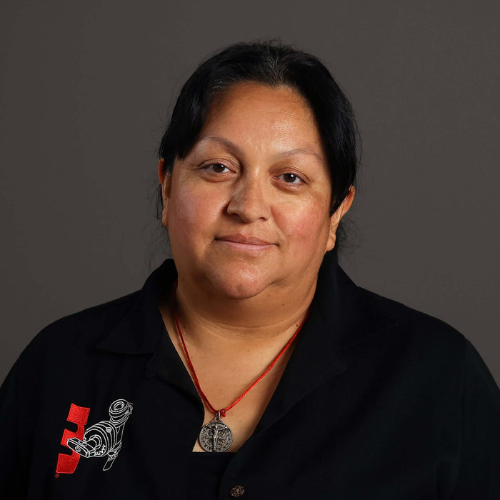 Portrait of a woman wearing a black shirt with a necklace, smiling against a dark background.