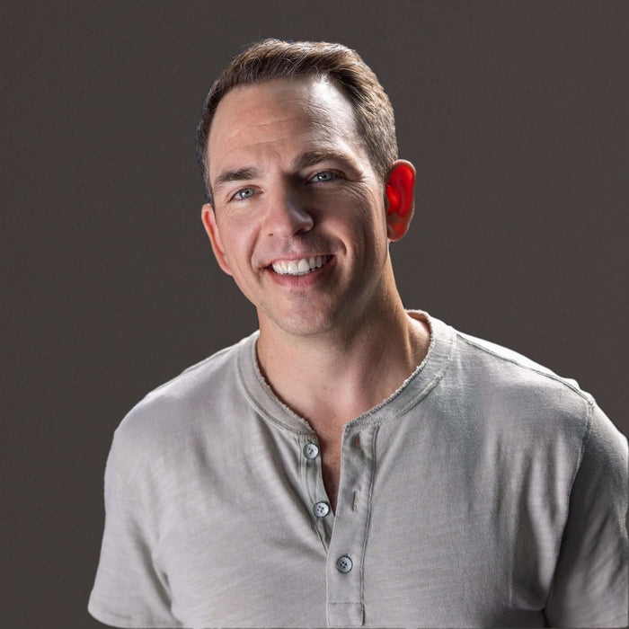 Smiling man wearing a gray henley shirt against a dark background, showcasing a friendly and approachable demeanor.