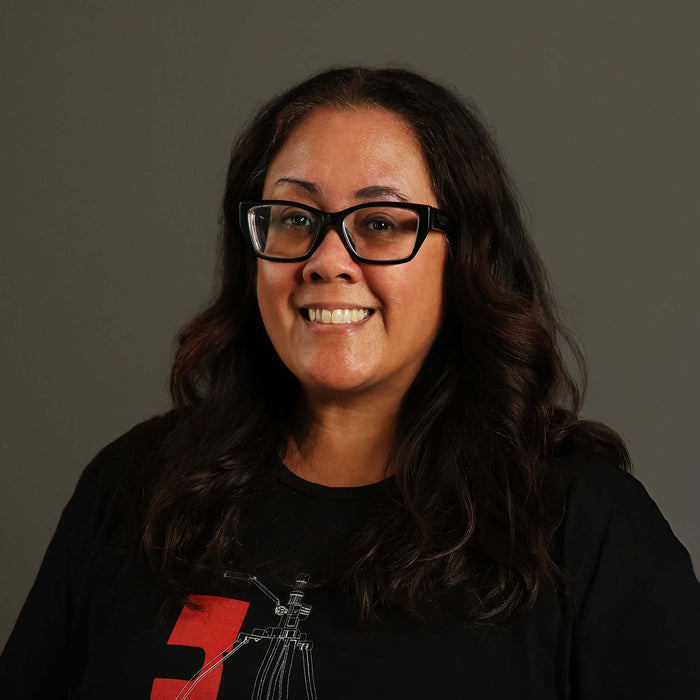 woman with glasses smiling in a black t-shirt, with long hair against a gray background