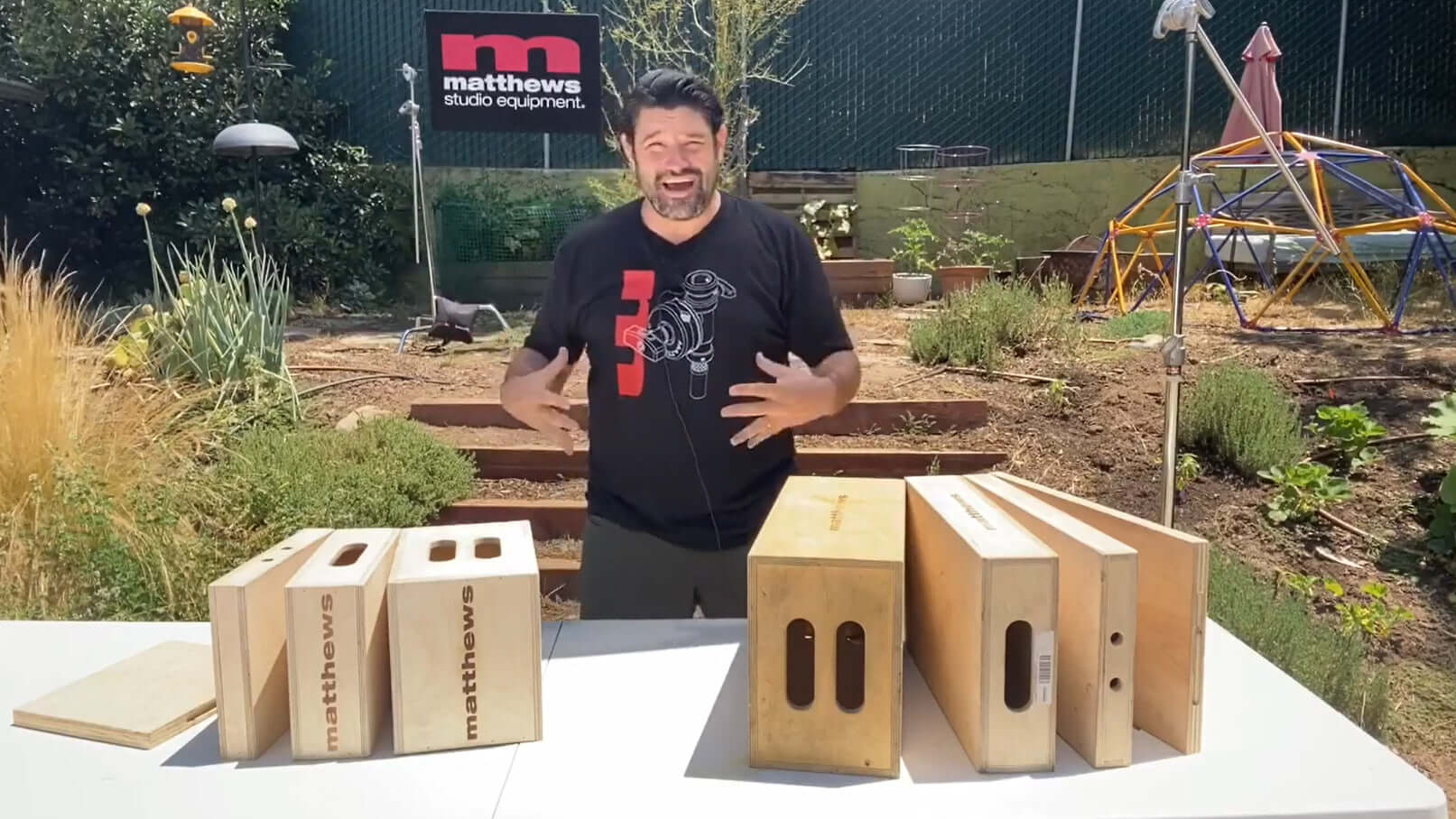 Person showcasing Matthews studio equipment in a garden setting with various sizes of wooden boxes on a table.