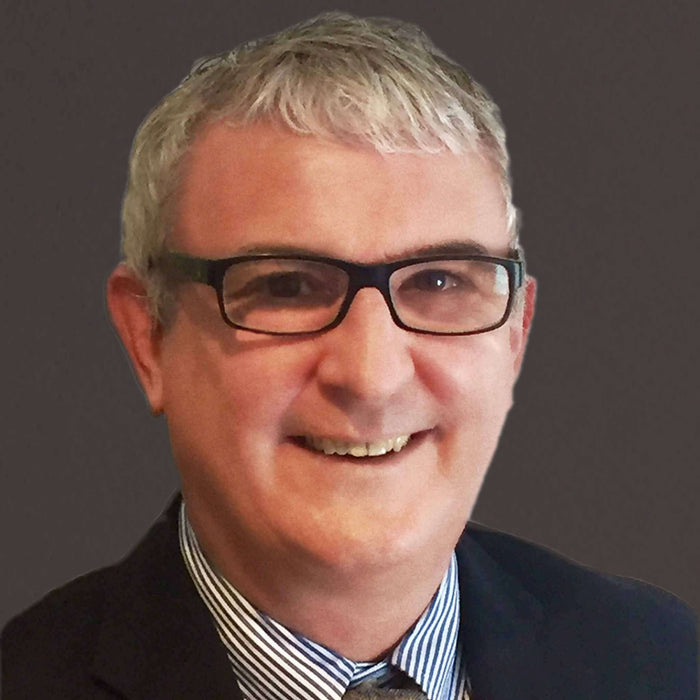 Professional man with glasses and gray hair, smiling against a dark background, exuding confidence and approachability.