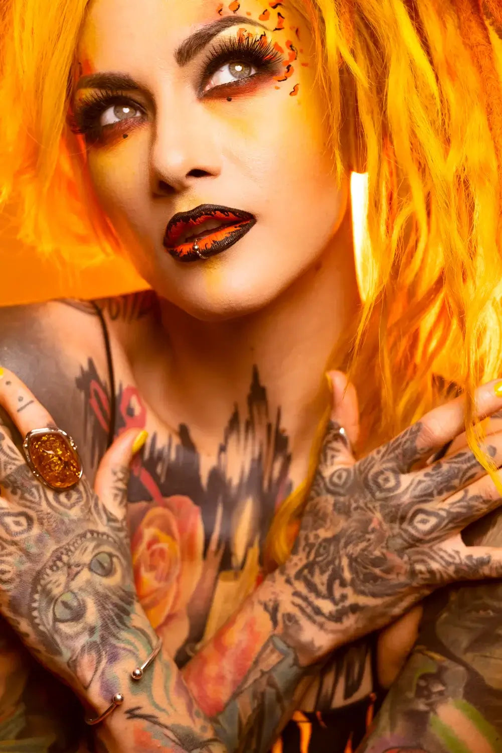 Bold portrait of a tattooed woman with vibrant orange hair and striking makeup, showcasing intricate body art and jewelry.