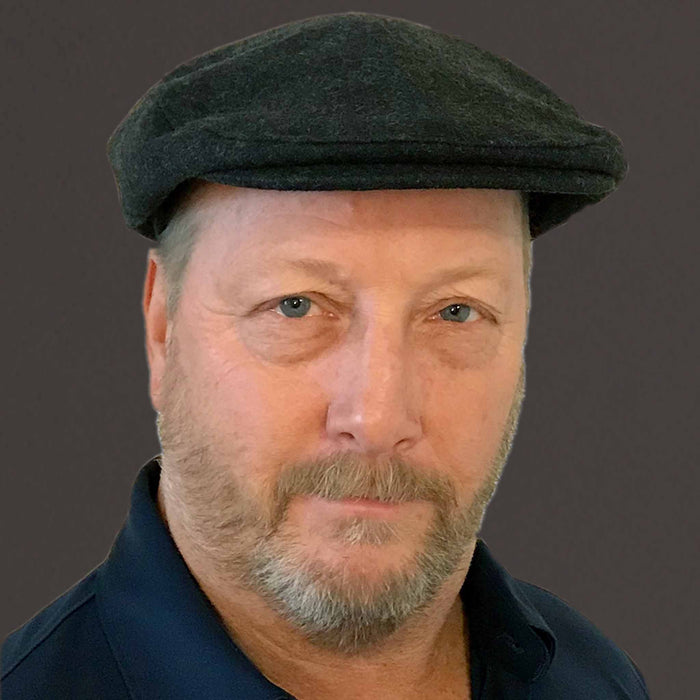 Man wearing a flat cap with a serious expression, set against a dark background.