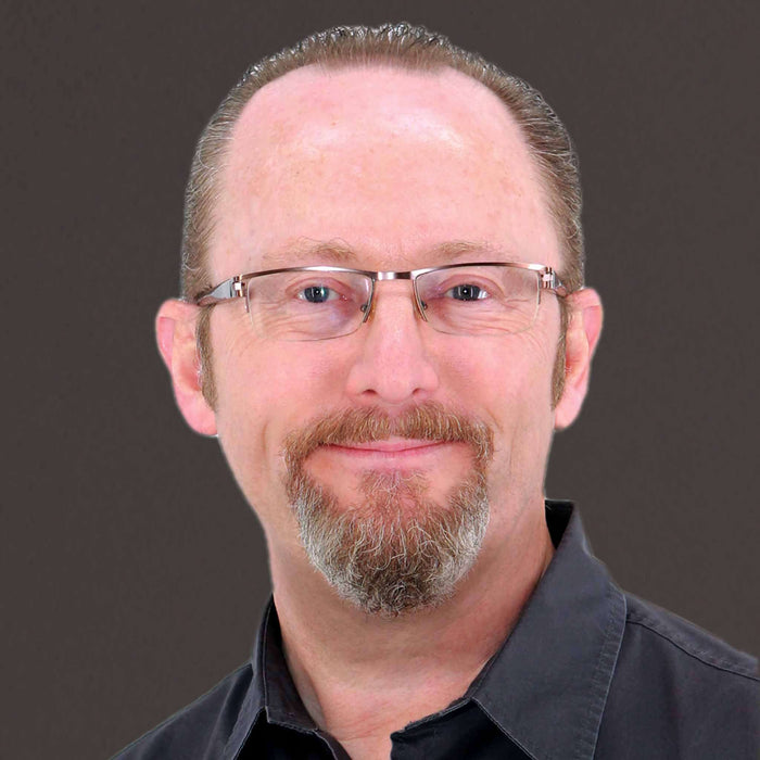 Professional headshot of a man with glasses and a beard, smiling against a dark background.