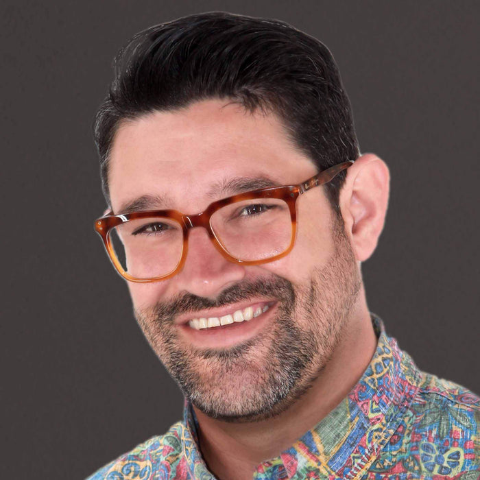 Smiling man with glasses wearing a colorful patterned shirt against a neutral background.