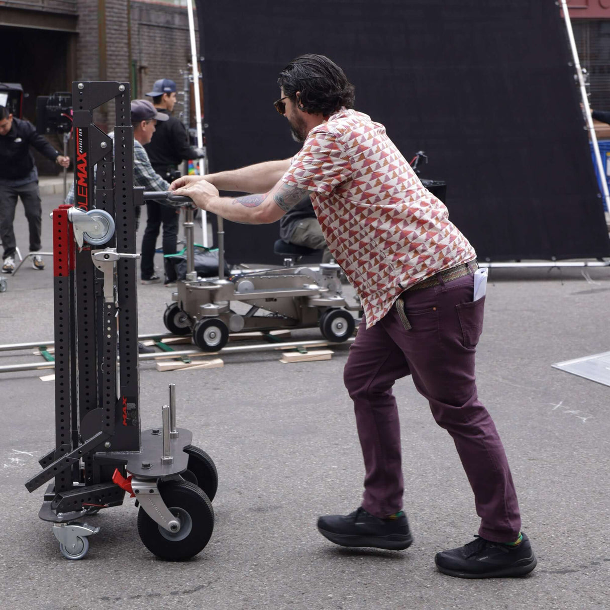 Man pushing Middle MAX Menace Arm support stand on a film set during production