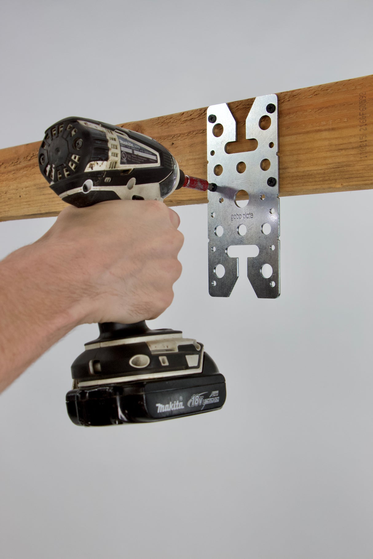 Hand using a drill to attach a Gobo Plate mounting adapter to a wooden beam for versatile equipment compatibility.